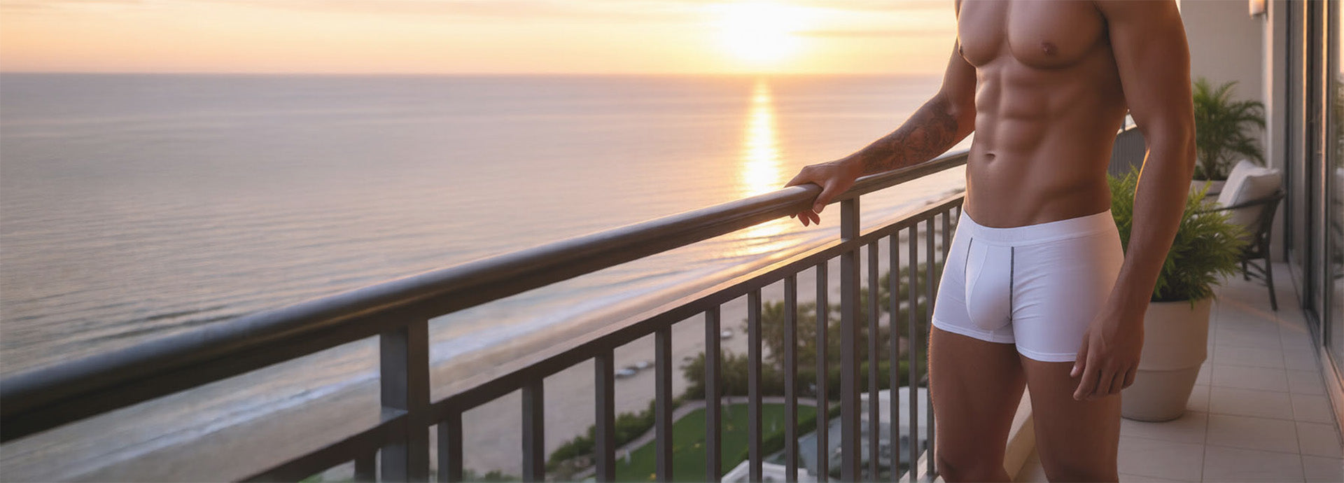 Man in comfort pouch underwear standing on a balcony overlooking the ocean at sunset
